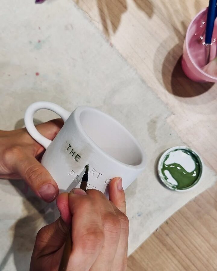 Atölyede bir seramik kupanın üzerine fırçayla elle yazı boyanıyor