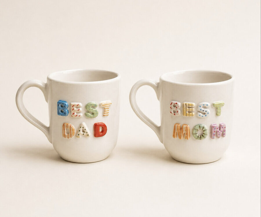 Renkli kabartma harflerle BEST DAD ve BEST MOM yazan iki beyaz seramik kupa